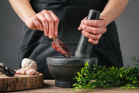 A female cook putting chilli pepper in a mortar