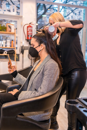 A hairdresser in a mask giving the final touches to the brunette client's hairstyle - new normalの写真素材
