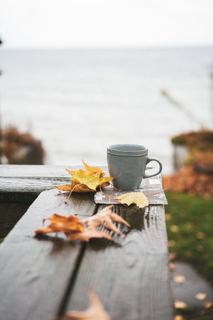 A vertical shot of a cup on the wooden balcony railing with dried leavesの写真素材