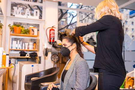 A hairdresser with a protective mask working in a beauty salon. Security measures of hairdressers in the Covid-19 pandemicの写真素材
