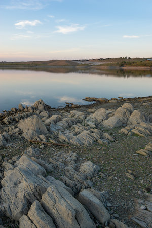 Lucefecit Dam in Terena with reflection on the lake reservoir and rocks on the foreground, in Portugalの写真素材