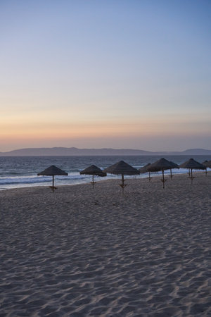 Empty beach at sunset in Comporta, Portugal with straw summer umbrellasの写真素材