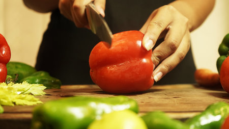 A woman cutting red pepper and other fresh vegetables on a chopping boardの写真素材