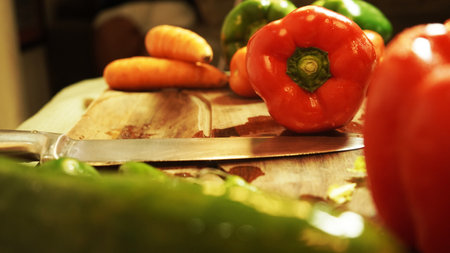 A lettuce, red paprika, and carrots with a sharp knife placed on a wooden surfaceの写真素材
