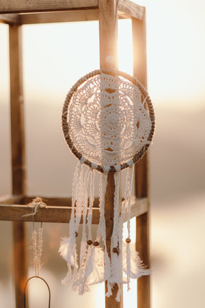 A vertical shot of a handmade dreamcatcher hanging on a block of wood during sunset