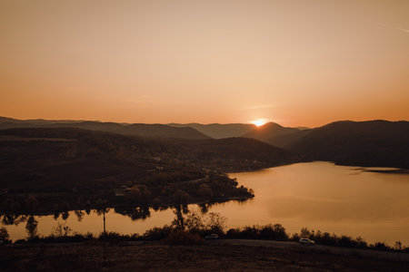 The beautiful sunset behind the forested mountains near the calm lake
