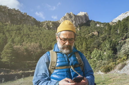 A portrait of a bearded explorer man walking through the mountains, using the map of his mobile phoneの写真素材