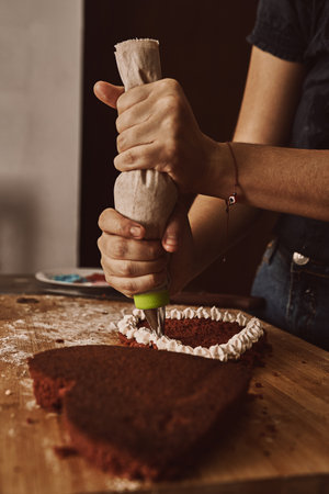 A woman's hand putting frosting on her heart-shaped cake in a kitchen