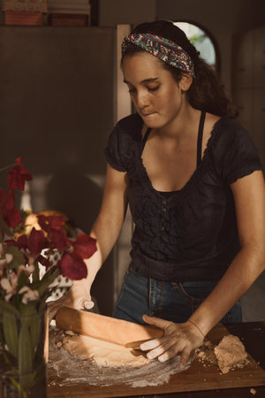 A Hispanic woman kneading the dough with a rolling pin on a wooden surfaceの写真素材