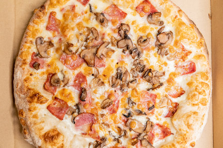A top view of a delicious pizza with mushrooms, cheese, bacon, and sauces in a boxの写真素材