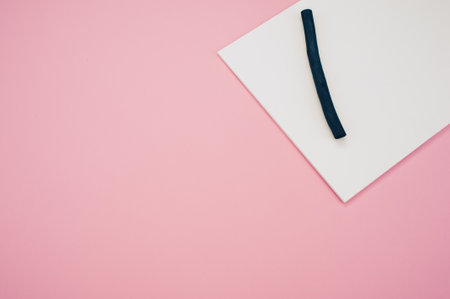 A top view closeup of a black piece of paper and a piece of black string on a pink backgroundの写真素材
