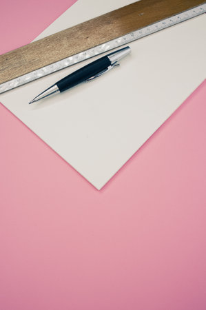 A top view closeup of a black piece of paper, ruler, and a pen on a pink backgroundの写真素材