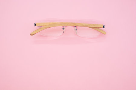 A top view closeup of glasses with wooden temples placed upside down on a pink backgroundの写真素材