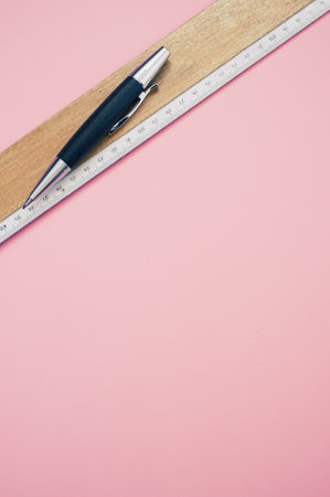 A top view closeup of a wooden ruler, and a pen placed on a pink backgroundの写真素材