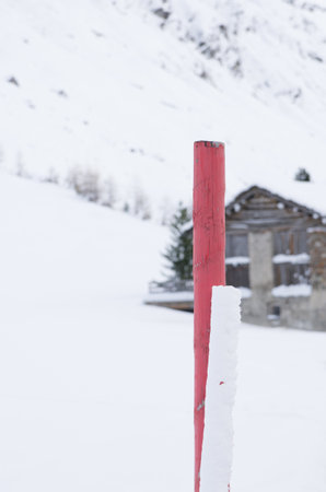 A closeup view of a wooden pole colored in red put in snow and the wooden house in the backgroundの写真素材