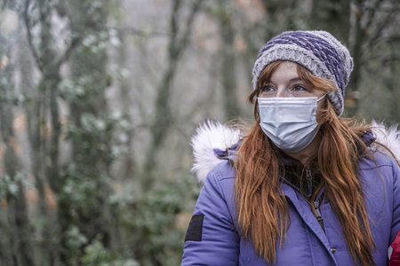 A redhead woman wearing a mask and walking in the park