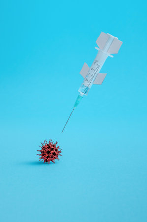 A vertical shot of a syringe and Covid-19 virus on a blue background - the concept of Covid-19 vaccineの写真素材