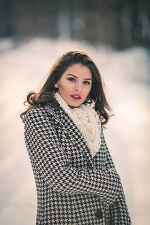 A shallow focus shot of a beautiful Caucasian woman wearing a coat posing in the snowy forest
