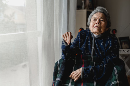 An old sick woman sitting in a wheelchair at homeの写真素材