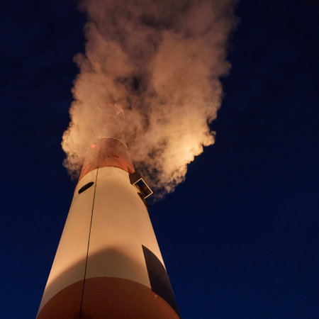 A night shot of white steam emitted from a striped pipeの写真素材