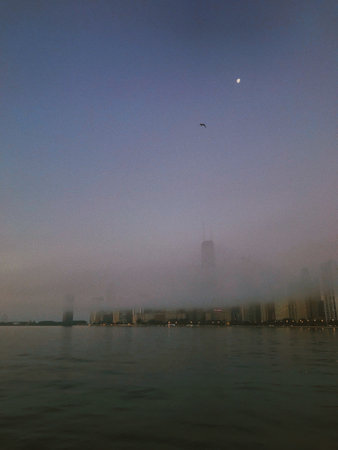 A vertical shot of an urban waterfrontcity skyline shouded in a dense fog at nightの写真素材