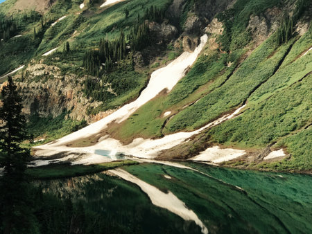 A majestic view of a grassy spring mountain with patches of melting snow and a reflective lake water