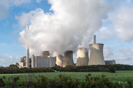 A green grassy land with clouds of smoke rising from the nuclear power plant in the background