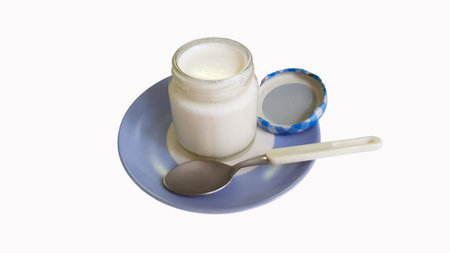 A closeup shot of an opened yogurt tub on a blue-white plate with a small spoon and a round lid on the white backgroundの写真素材