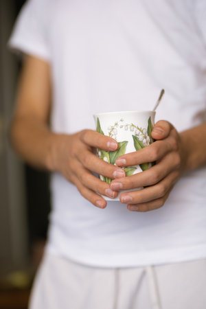 A man wearing white clothes holding a floral mugの写真素材