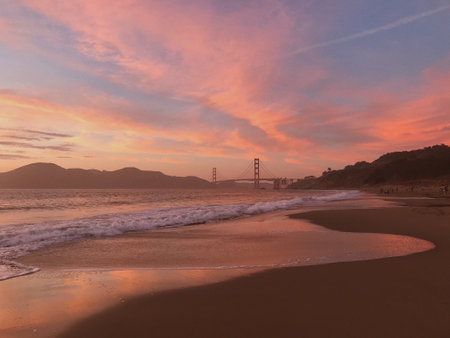A majestic pink sunset cloudscape over wavy seawater with the Golden Gate Bridge on the horizonの写真素材
