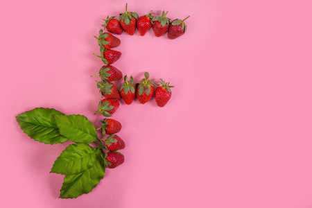 A top view of the F letter made of fresh strawberries on pink backgroundの写真素材