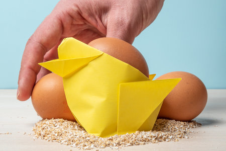 A closeup of a person putting eggs on a wooden table with an origami chick and oats on it