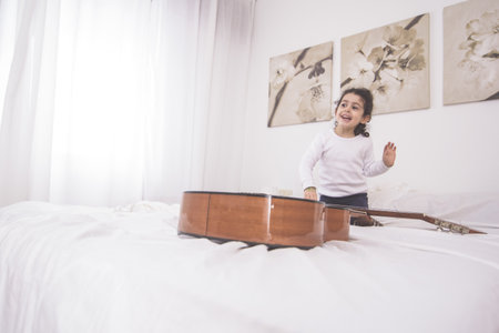 A female child playing with an acoustic guitar on a bedの写真素材