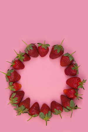 A top view of a beautiful circular frame made of strawberries on a pink backgroundの写真素材