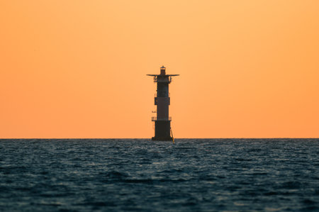 A beautiful view of a lighthouse in the sea against a golden sunset skyの写真素材