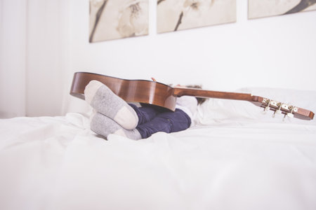 A closeup shot of a cute Caucasian little girl lying on a bed with a guitar on herの写真素材