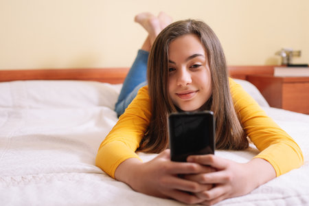 A young girl with her smartphone lying on bedの写真素材