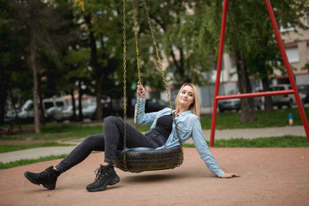 A shallow focus of an adult blonde woman on a tire swing in a playground in Bosnia and Herzegovina