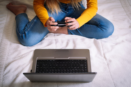 A thigh angle shot of a girl with joysticks in her hands in front of a laptop on bed