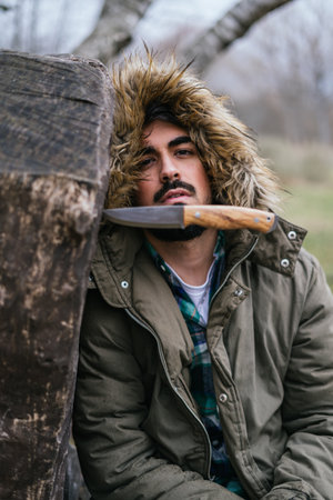 A vertical selective focus shot of a knife in a log with a male in the background