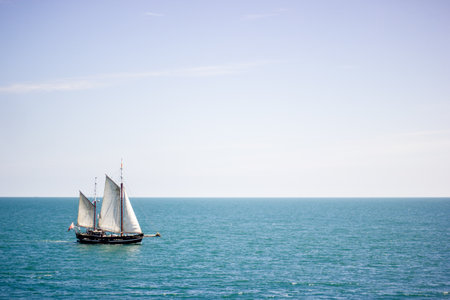 A sailing boat with white sails on a calm sea surface at daytime