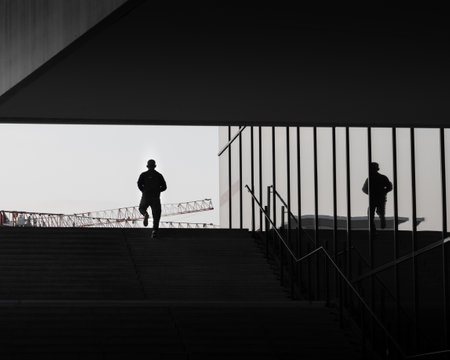 A grayscale shot of a person walking up the stairs near a reflective buildingの写真素材
