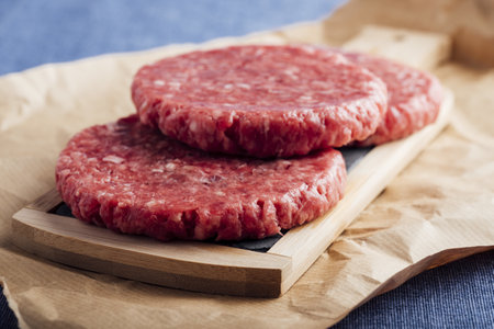 A closeup shot of fresh raw burger patties on a wooden boardの写真素材