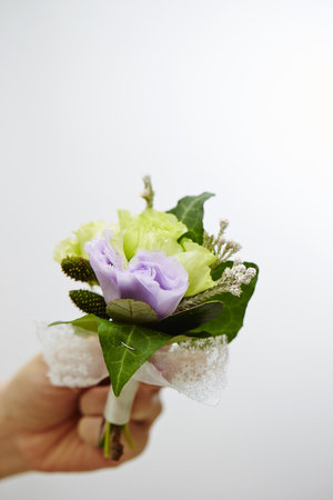A vertical shot of a hand holding a Buttonhole for the groom on a white background