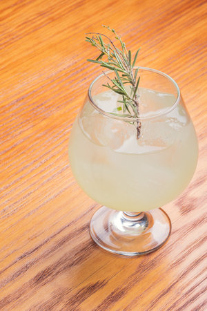 A vertical closeup shot of a refreshing alcoholic drink with rosemary on a tableの写真素材