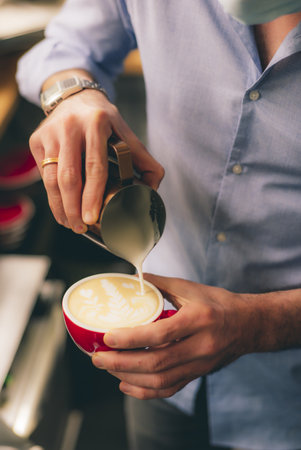 A handsome barista with a face mask making a cup of coffee at the coffee shopの写真素材