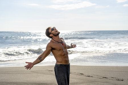 An excited shirtless man on the beach washed by ocean wavesの写真素材
