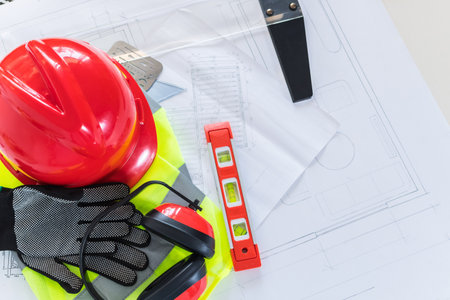 An architect engineer Work desk with blueprints, rulers, tools, helmet, yellow safety vest.の写真素材
