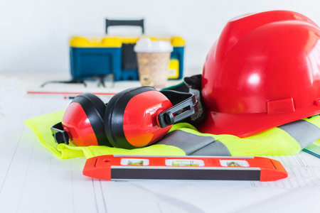 An architect-engineer Work desk with blueprints, rulers, tools, helmet, yellow safety vest.