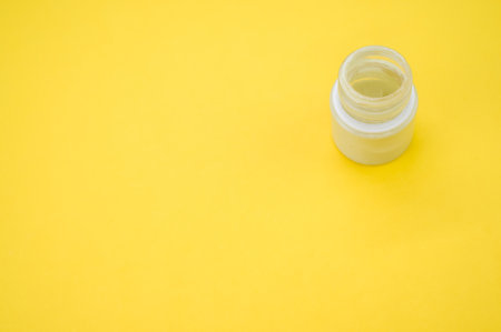A high angle shot of a small can of white gouache paint on a yellow backgroundの写真素材